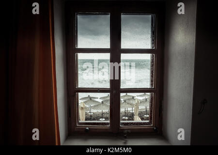 Spettacolare vista sul mare dalla finestra aperta con grandi onde tempestose e drammatico cielo durante la pioggia e la tempesta meteo in caduta stagione sulla costa del mare Foto Stock