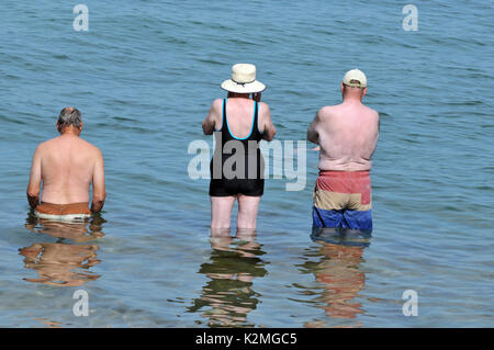 Tre anziani o persone in pensione due uomini una donna in piedi nel mare andando a nuoto con la schiena per la telecamera il pensionamento in pensione salute attività Foto Stock