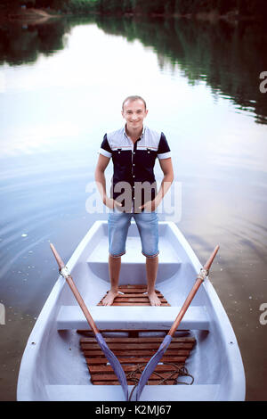 Giovane ragazzo in piedi la barca bianca, uomo bello luce in pantaloncini e maglietta, adolescente gode di attività ricreative all'aperto Foto Stock