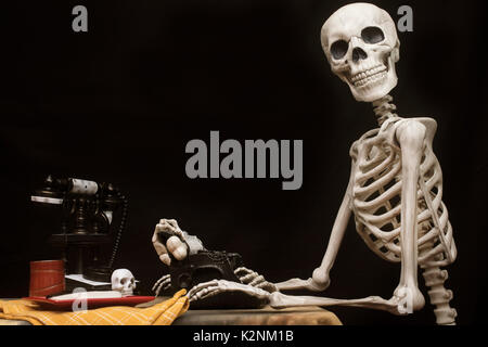 Umano scheletro di Halloween con una macchina da scrivere, telefono e cookie su una piastra Foto Stock