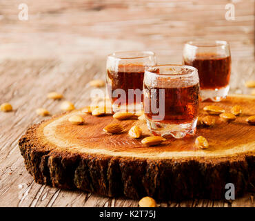 Liquore italiano Amaretto in tazze con mandorle su una tavola di legno, fuoco selettivo Foto Stock