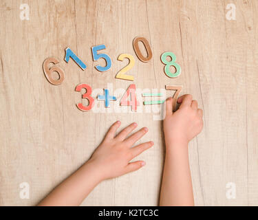 Le mani del bambino con una semplice equazione matematica contro il tavolo di legno Foto Stock