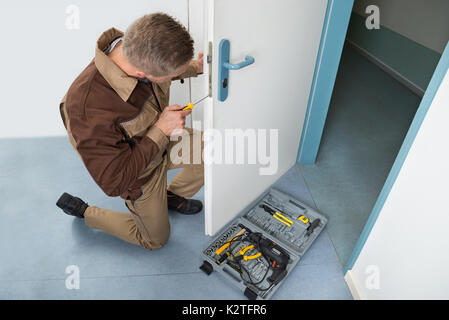 Angolo di Alta Vista del falegname maschio con un cacciavite il fissaggio serratura della porta Foto Stock