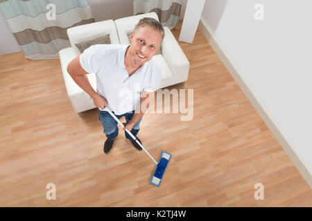 Giovane uomo felice piano di pulizia con Mop in casa Foto Stock