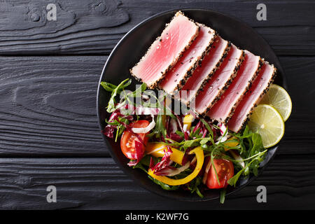 Close up di rara disseccata Ahi le fette di tonno fresco con insalata di verdure su una piastra. Vista in pianta da sopra la linea orizzontale Foto Stock