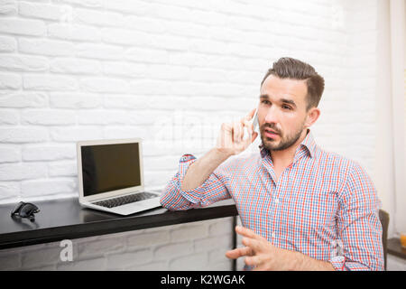 Giovane uomo di effettuare i negoziati entro il telefono nel suo ufficio di casa. Foto Stock