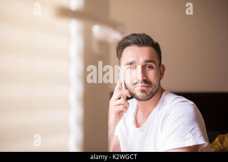 Uomo che parla al telefono in camera da letto Foto Stock