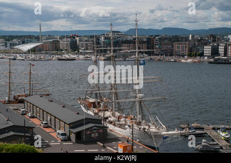 La zona del molo Aker Brygge si vede attraverso il fiordo con la scuola vela Christian Radich in primo piano, Oslo, Norvegia. Foto Stock