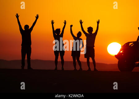 Felici turisti guardando il tramonto tra le dune di sabbia del deserto vicino a Huacachina Oasis, Ica, Perù, Sud America (MR) Foto Stock