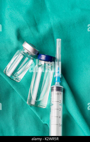 Siringa medica e fiale giacente sull'ospedale sfondo verde. Lo sfondo può essere una parte di tessili di un medico o un infermiere uniforme di lavoro Foto Stock
