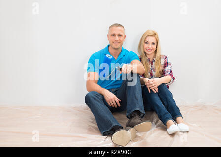 Giovane seduto sul pavimento a sorridere di fronte parzialmente parete dipinta in Home Foto Stock