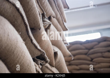 Canapa vecchia i sacchi contenenti il chicco di caffè in magazzino. accatastati sacchi in magazzino. Foto Stock