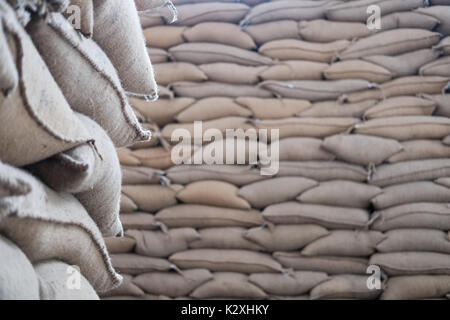 Canapa vecchia i sacchi contenenti il chicco di caffè in magazzino. accatastati sacchi in magazzino. Foto Stock