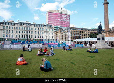 I giovani seduti sul prato in George Square Glasgow sotto le persone fanno Glasgow banner Foto Stock