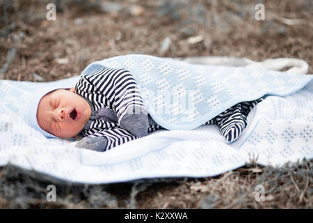 Sbadigliare neonato giace su blu coverlet in erba. Foto Stock