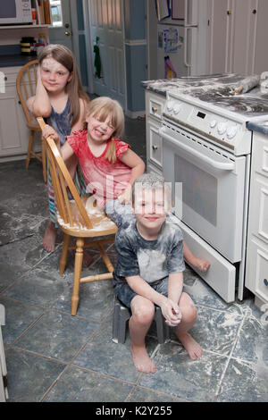 Tre bambini cattivi che hanno appena fatto un pasticcio in cucina sedersi accanto al forno cercando felice Foto Stock