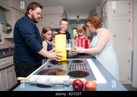 Una famiglia di cinque persone la cottura della torta di mele in cucina. Foto Stock