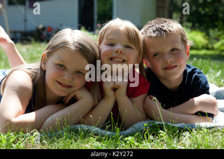 Sorridente due sorelle e un fratello che giace nell'erba. Foto Stock