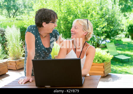 Due belle donne mature amici utilizzando laptop, sulla terrazza del giardino Foto Stock