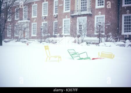 Tre colorate sedie di prato stand coperto in tre metri di neve nella parte anteriore di un edificio in mattoni su un quad nevoso alla Johns Hopkins University, Baltimora, Maryland, 2016. Foto Stock