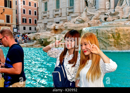 Due giovani donne giapponesi che si esibiscono per una foto di fronte alla Fontana di Trevi. Una donna con capelli sbiancati. Turisti, amici in viaggio. Roma, Italia Europa Foto Stock