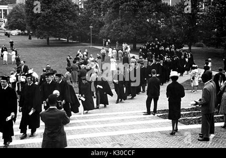 Il giorno d'inizio, una lunga fila di laureati e facoltà che indossano cappucci neri e gli abiti trasportare opuscoli laminati mentre procedono in Shriver Hall, come membri della famiglia di scattare foto sul prato, Johns Hopkins University, Baltimora, Maryland, 11 giugno 1963. Foto Stock