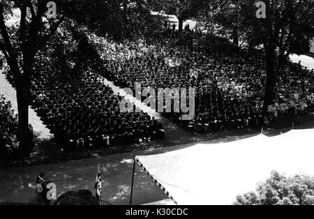 Il giorno d'inizio, centinaia di laureati che indossano cappucci neri e gli abiti sit in file ordinate su un ombroso Wyman del quadrangolo durante la cerimonia, guardare gli eventi sul palcoscenico bianco davanti, Johns Hopkins University, Baltimora, Maryland, 11 giugno 1957. Foto Stock