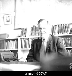 George Francis Carter, professore di geologia presso la Johns Hopkins University e la baia di Chesapeake studioso, siede alla sua scrivania davanti a una parete di libri e di una macchina da scrivere, sorridente, Baltimore, Maryland, 1959. Foto Stock