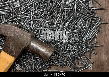 Martello sulla sommità di una pila di molti chiodi in acciaio, su una superficie di legno sfondo, primo piano Foto Stock