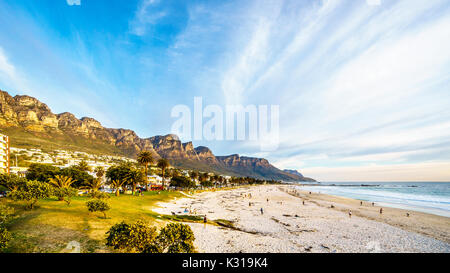 La spiaggia di Camps Bay vicino a Città del Capo in Sud Africa in una bella giornata invernale, con il retro della Table Mountain, chiamò i dodici apostoli, sulla sinistra Foto Stock