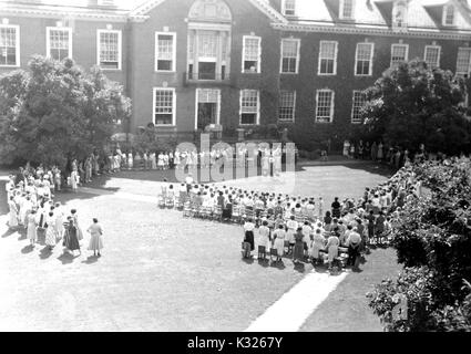 Alla fine dell'anno scolastico per una dimostrazione scuola presso la Johns Hopkins University, i genitori e gli insegnanti a stare di fronte di sedie in fila al di fuori di un edera-campus coperto edificio, attesa per le giovani ragazze e ragazzi per iniziare lo spettacolo si esibiranno per chiudere l'anno, nell'erba su quadrangolo in una giornata di sole, Baltimore, Maryland, luglio 1950. Foto Stock