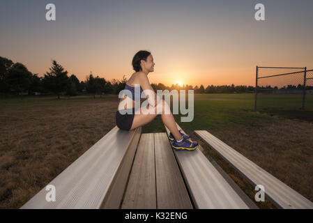Una femmina di runner si prende una pausa sul bleechers al tramonto. Foto Stock