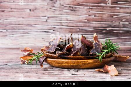 Tirata di carne, mucca, cervi, belva o biltong in ciotole di legno su un tavolo rustico, il fuoco selettivo Foto Stock