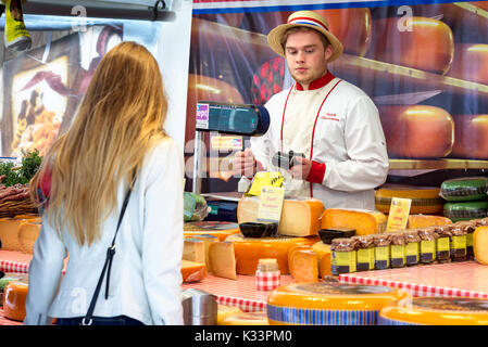 Kristiansand, Norvegia - 16 agosto 2017: Travel documentario di strada del mercato. Fornitore di formaggio in Olandese Cheeseman femmina con il cliente. Il fornitore tiene credi Foto Stock