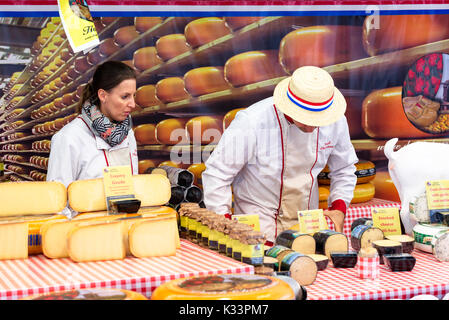 Kristiansand, Norvegia - 16 agosto 2017: Travel documentario di strada del mercato. I fornitori di formaggio circa per sollevare un pezzo di formaggio affumicato dall'assortimento Foto Stock