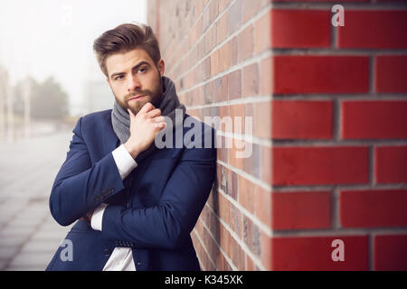 La foto di un giovane uomo che indossa navy tuta e scialle. Lui è appoggiata contro un muro di mattoni e pensando a qualcosa. Foto Stock