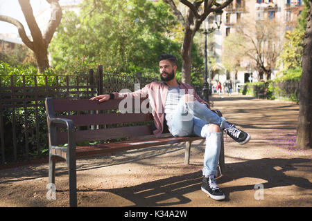 La foto di un giovane uomo seduto sulla panchina del parco e godendo il suo tempo libero. Foto Stock