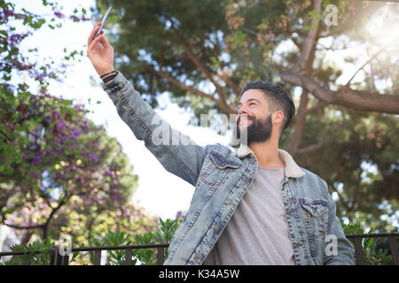 Una foto di giovani, uomo bello in piedi sul vicolo al parco e tenendo lo stesso una foto. Foto Stock