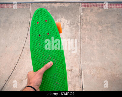 Maschio lato tenendo un penny verde pensione in uno skatepark. Foto Stock