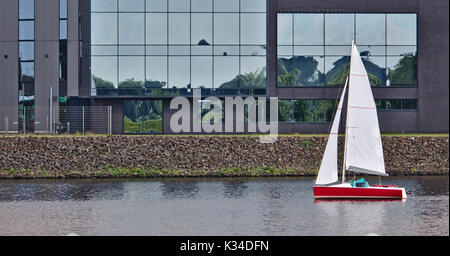Rosso barca a vela vela passato a waterfront edificio per uffici Foto Stock
