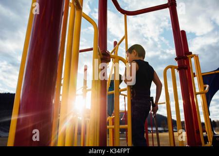 Un bambino gioca su attrezzature per parchi giochi al tramonto. Foto Stock