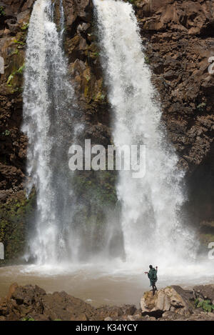 Uomo del posto in piedi nella spruzzata di una cateratta di Tis Abay (cascate del Nilo Azzurro), vicino a Bahir Dar, Etiopia Foto Stock
