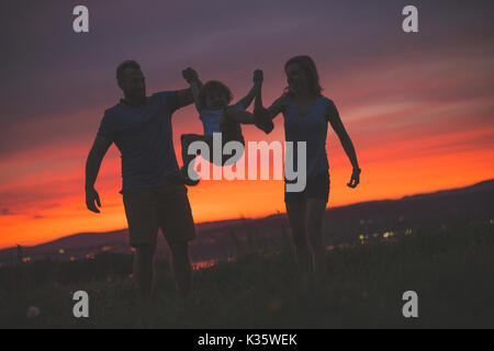 La madre e il padre il figlio oscillanti in aria al tramonto Foto Stock