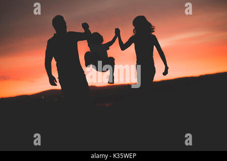 La madre e il padre il figlio oscillanti in aria al tramonto Foto Stock