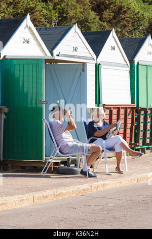 Bournemouth, Dorset, Regno Unito. 2 settembre 2017. Tempo nel Regno Unito: Bella calda giornata di sole a Bournemouth spiaggia come i visitatori arrivare presto per ottenere un buon posto il terzo giorno del Bournemouth Air Festival. Coppia seduta rilassante al sole fuori dalla capanna sulla spiaggia - uomo che guarda attraverso binocoli, donna con rivista. Credit: Carolyn Jenkins/Alamy Live News Foto Stock