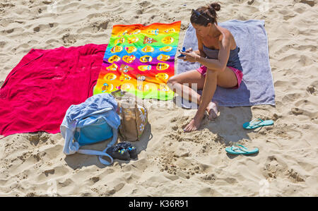 Bournemouth Dorset, Regno Unito. 2 Sep, 2017. Regno Unito: meteo bella calda giornata di sole a Bournemouth Beach. Donna seduta su asciugamano tramite telefono cellulare iPhone cellulare smartphone. Credito: Carolyn Jenkins/Alamy Live News Foto Stock