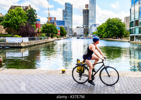 Un ciclista in shorts, gilet e casco che cavalcano una bicicletta sull'alzaia del canale di Regent a City Road Basin, Islington, Londra, UK, in una calda giornata estiva Foto Stock