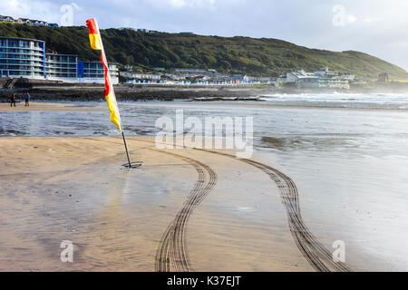 Rosso e giallo di avvertimento bandiera e tracce di pneumatici da RNLI veicolo sulla spiaggia di sabbia con la bassa marea, Condino, Devon, Inghilterra, Regno Unito Foto Stock