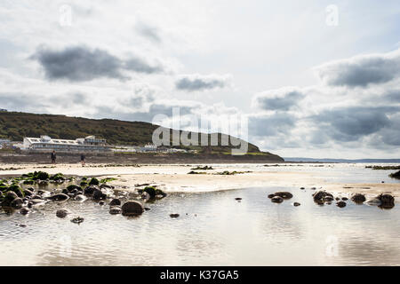 Bassa angolazione della spiaggia sabbiosa a Condino, Devon, Inghilterra, Regno Unito, con la bassa marea con riflessi del cielo e delle nubi in piscine di roccia Foto Stock