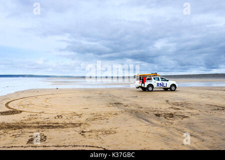 Bianco bagnino RNLI veicolo e tracce di pneumatici sulla spiaggia sabbiosa a bassa marea, Condino, Devon, Inghilterra, Regno Unito Foto Stock